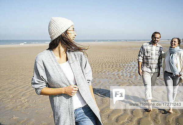 Young woman laughing looking at man and mother walking in background at beach