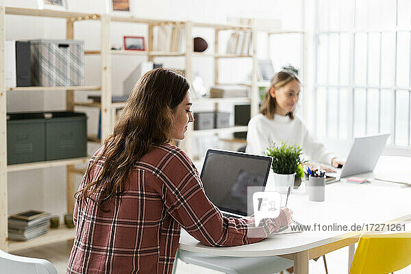 Woman using laptop with businesswoman sitting in background at office