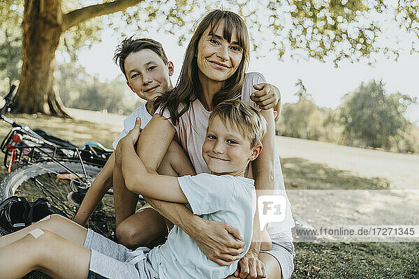 Mutter umarmt ihre Söhne  während sie in einem öffentlichen Park sitzen