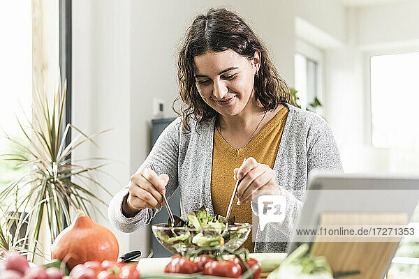 Lächelnde Frau macht Salat  während sie zu Hause am Tisch steht