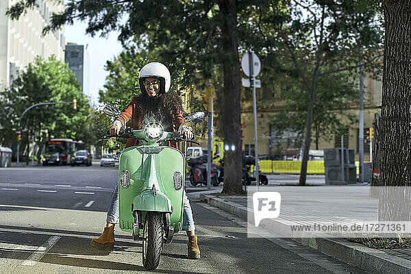 Lächelnde junge Frau fährt Motorroller auf der Straße in der Stadt