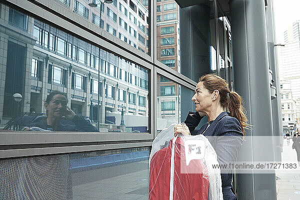 Geschäftsfrau mit Kleidung  die ihr Spiegelbild betrachtet  während sie in der Stadt steht
