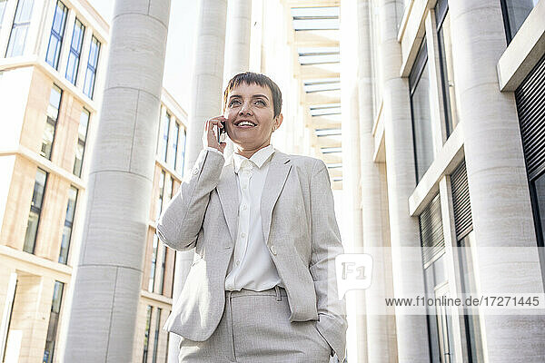 Frau  die mit einem Mobiltelefon spricht  während sie vor einem Bürogebäude steht