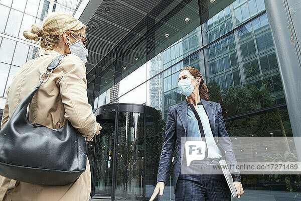 Reife Frauen mit Gesichtsmaske im Gespräch  während sie vor einem Bürogebäude stehen