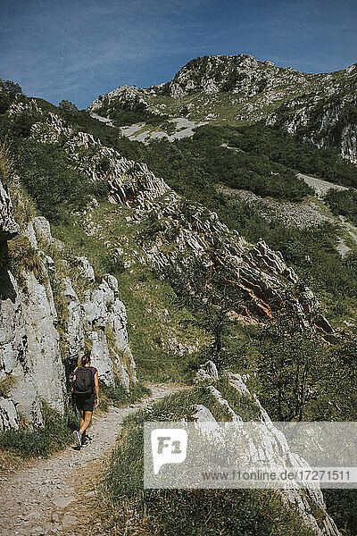 Frau  die an einem sonnigen Tag auf einem Wanderweg bei einer Felsformation spazieren geht