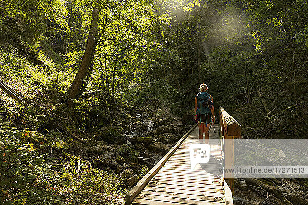 Wanderin beim Überqueren einer Holzbrücke  die sich im Sommer über einen Waldbach spannt