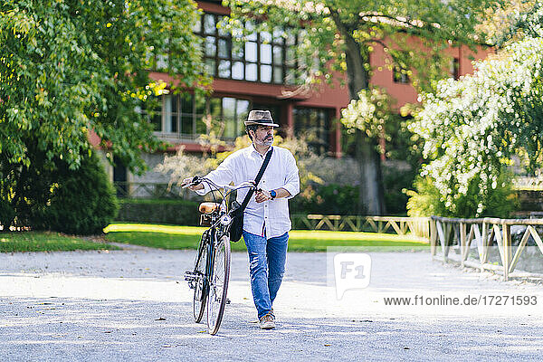 Älterer Mann mit Fahrrad auf dem Fußweg in einem öffentlichen Park