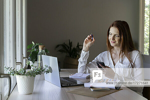 Lächelnde Frau  die ein Handy und einen Fidget Spinner benutzt  während sie zu Hause sitzt