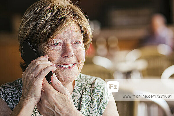 Smiling woman talking on mobile phone while sitting at cafe