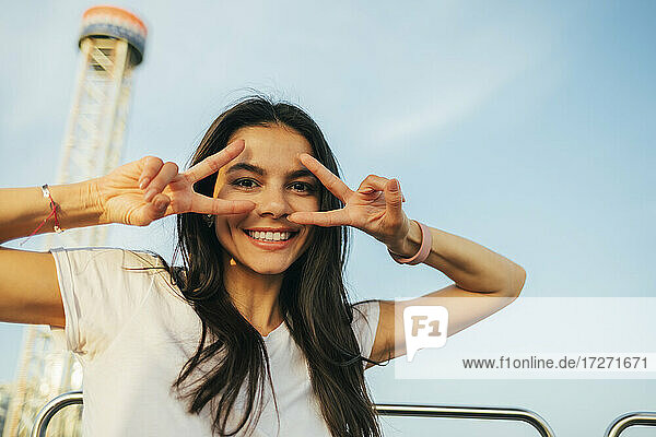 Smiling beautiful woman showing peace sign while enjoying Ferris wheel ride at sunset