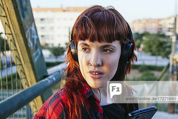 Nachdenkliche junge Frau  die wegschaut  während sie über Kopfhörer Musik hört