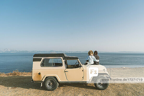 Paar bewundert den Meerblick  während es mit seinem Hund auf einem Auto am Strand sitzt
