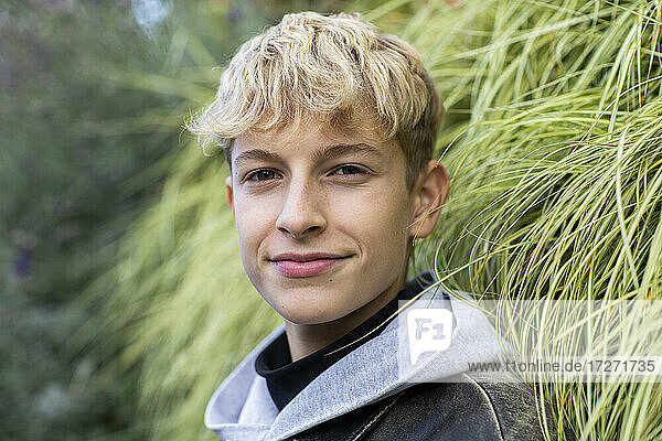 Confident blond teenage boy standing against plants