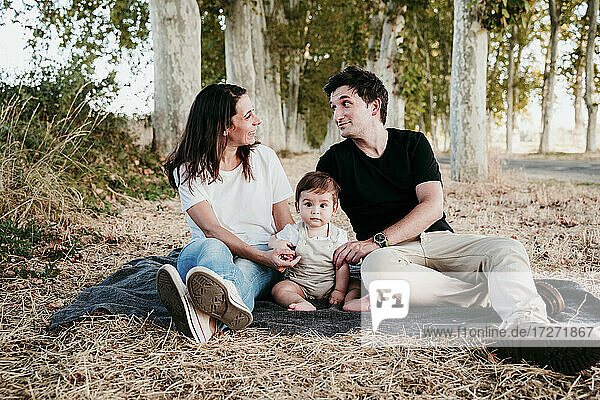 Couple talking while sitting with baby boy on blanket outdoors