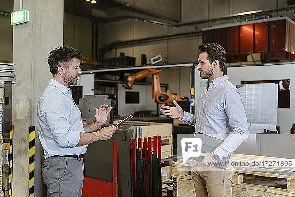Businessman with digital tablet discussing with colleague while standing at factory