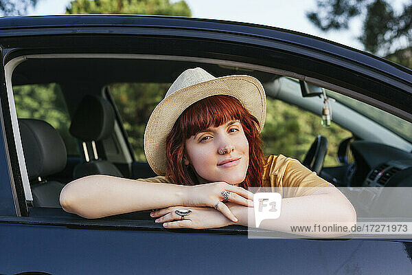 Smiling young beautiful redhead woman leaning out from car window