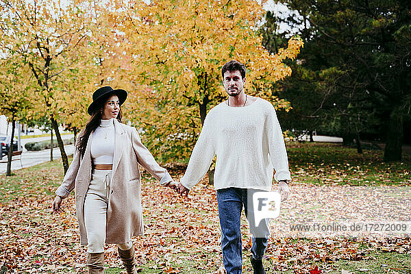 Smiling young couple holding hands against tree during autumn