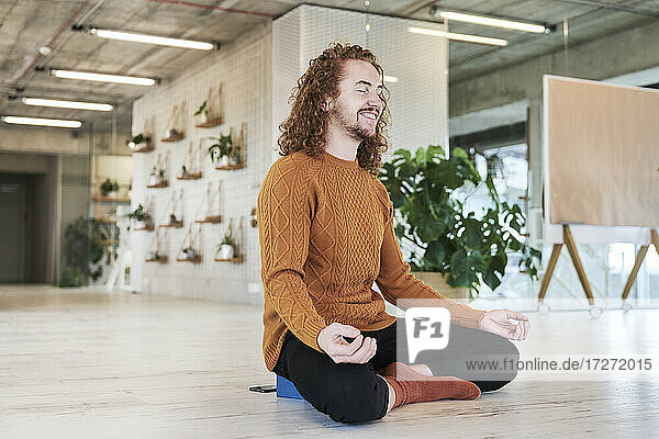 Lächelnder Mann meditiert auf dem Boden sitzend im Wohnzimmer zu Hause