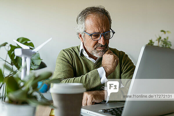 Mann mit Brille  der einen Laptop benutzt  während er zu Hause am Tisch sitzt