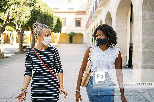 Frauen mit Gesichtsmaske unterhalten sich beim Spaziergang in der Stadt