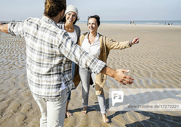 Mann steht mit ausgestreckten Armen am Strand und umarmt Frauen