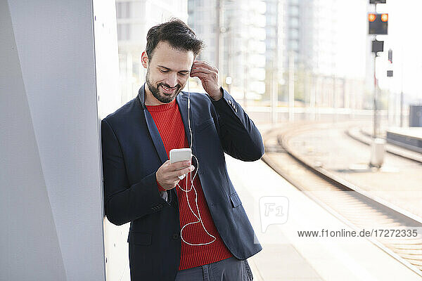 Lächelnder Unternehmer mit In-Ear-Kopfhörern auf dem Bahnsteig