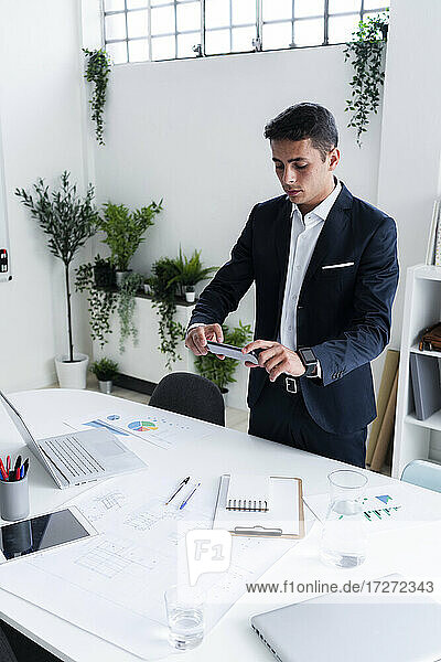 Gut aussehender männlicher Unternehmer  der seinen Schreibtisch im Kreativbüro fotografiert