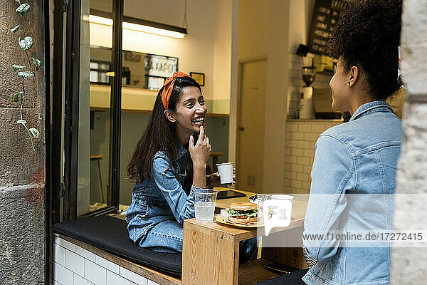 Lächelnde Frauen im Gespräch am Fenster eines Cafés