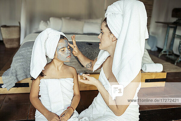 Frau beim Auftragen von Gesichtscreme auf das Gesicht ihrer Tochter  während sie zuhause sitzt