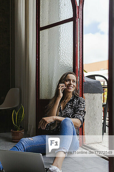 Lächelnde kreative Geschäftsfrau  die mit ihrem Handy telefoniert  während sie an der Tür im Büro sitzt