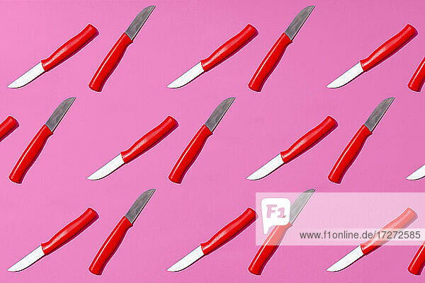Table knives arranged on pink background