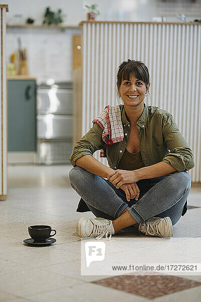 Lächelnde Besitzerin mit gekreuzten Beinen auf dem Boden sitzend in einem Cafe