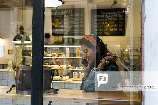 Lächelnde junge Frau  die in einem Café sitzt und mit ihrem Handy telefoniert