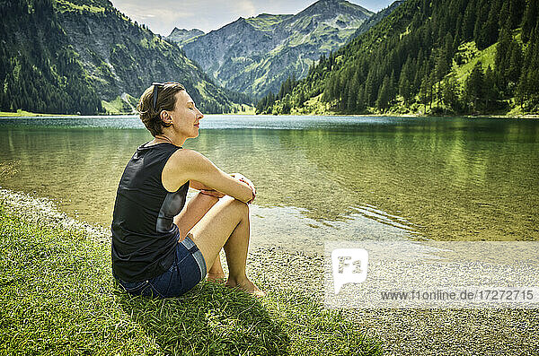Relaxed woman sitting with eyes closed at lakeshore on sunny day