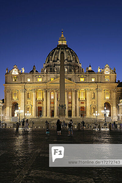 Touristen auf dem Petersplatz mit dem beleuchteten Petersdom bei klarem blauem Himmel in der Nacht  Vatikanstadt  Rom  Italien