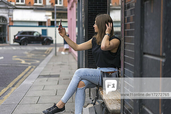 Junge Frau mit Händen in den Haaren nimmt Selfie auf Smartphone