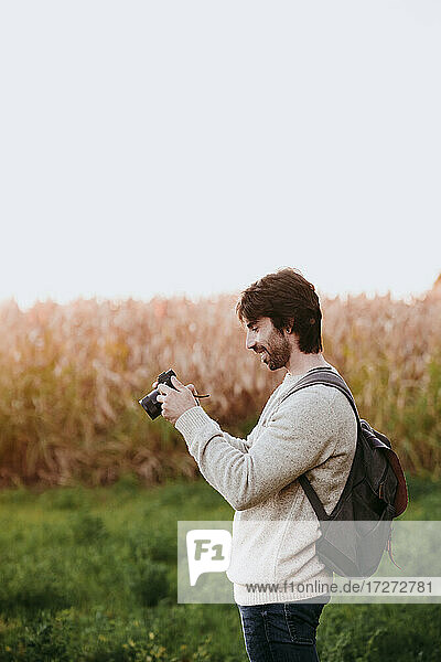 Mittlerer erwachsener Mann mit Rucksack  der eine Kamera hält  während er auf einem Feld steht