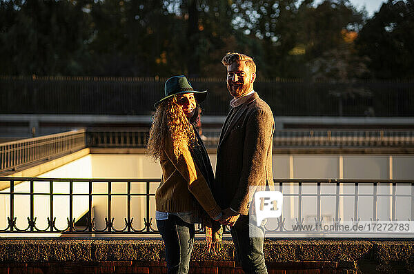 Verheiratetes Paar hält sich an den Händen  während es an einem Geländer in der Stadt steht