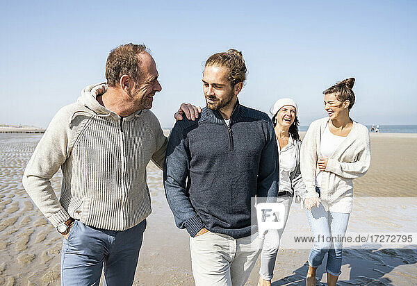 Männer unterhalten sich beim Spazierengehen mit Frauen im Hintergrund am Strand
