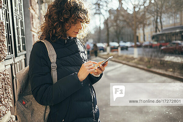 Mittlere erwachsene Frau mit Tasche  die ein Mobiltelefon benutzt  während sie auf dem Bürgersteig in der Stadt steht