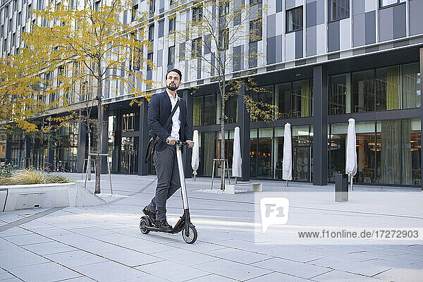 Businessman riding on electric scooter against building in city