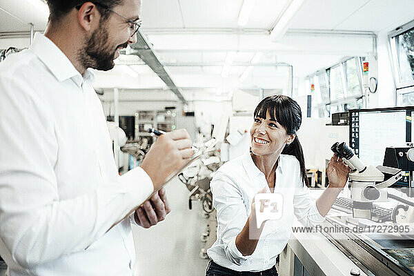 Lächelnde Technikerin im Gespräch mit einem männlichen Kollegen im Labor