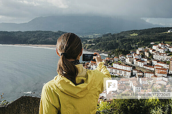 Rückansicht einer Frau  die im Urlaub mit dem Handy ein Dorf fotografiert