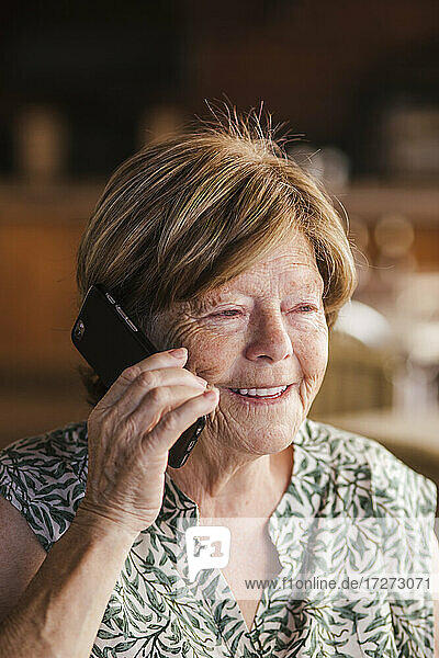 Senior woman smiling while talking on mobile phone at cafe