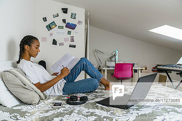 Teenager-Mädchen schreibt in ein Heft  während sie zu Hause auf dem Bett sitzt