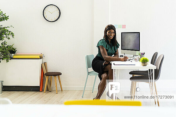 Lächelnde Geschäftsfrau am Schreibtisch sitzend bei der Arbeit im Büro