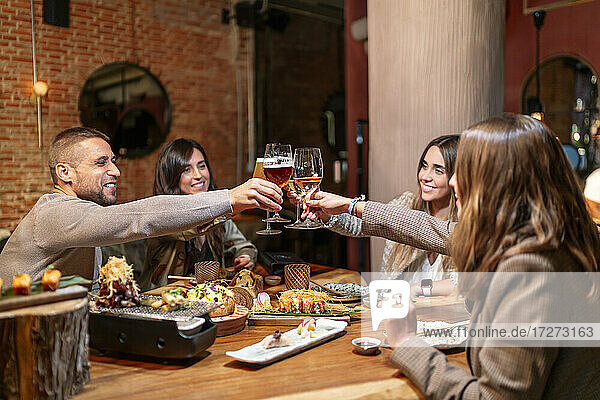 Smiling friends toasting drink while sitting by table at restaurant