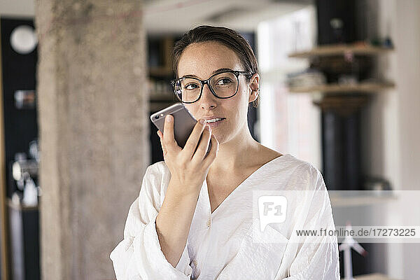 Geschäftsfrau  die im Büro stehend mit einem Mobiltelefon spricht