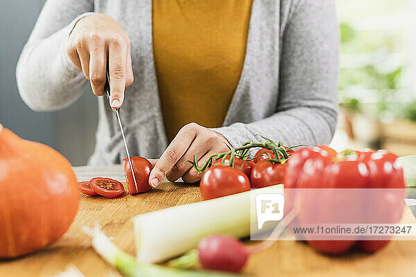 Junge Frau  die zu Hause am Tisch sitzend eine Tomate schneidet
