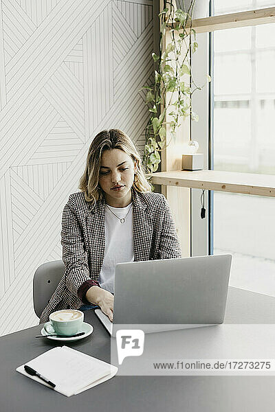 Junge Frau arbeitet am Laptop,  während sie in einem Café sitzt